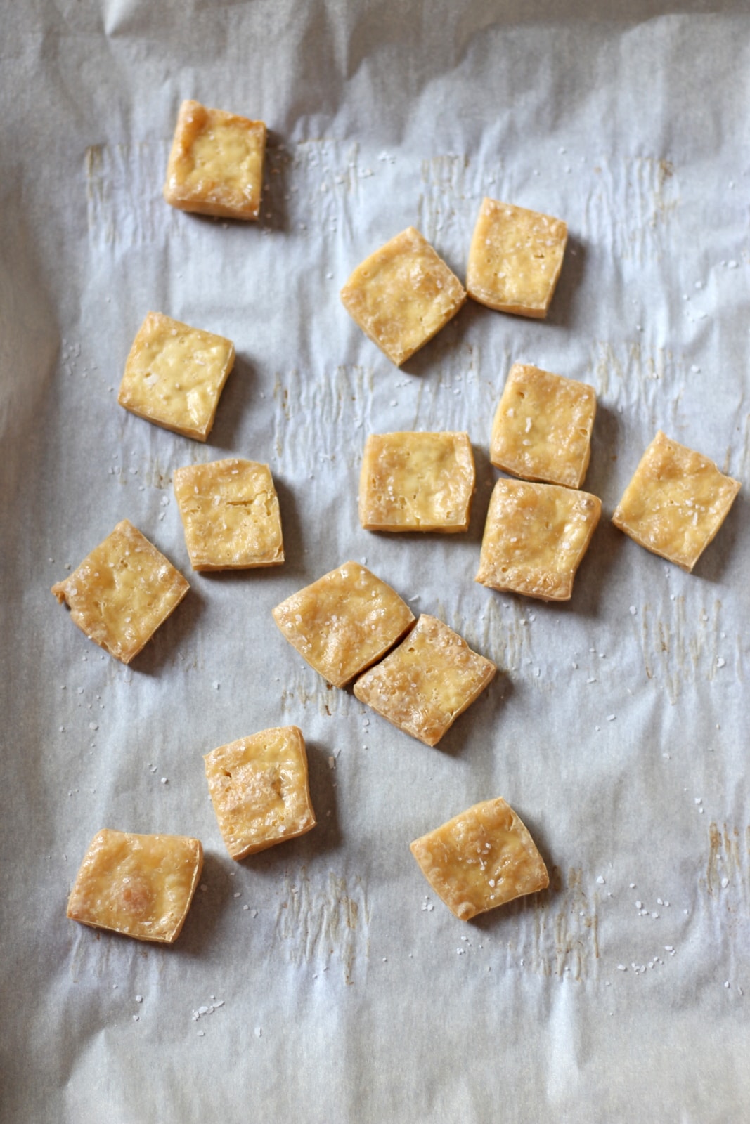 Several pieces of baked tofu on a parchment-lined baking sheet. 