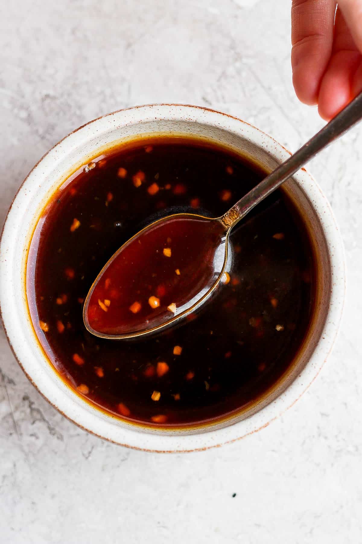 A bowl of homemade teriyaki sauce with someone pulling up a spoonful out of it. 