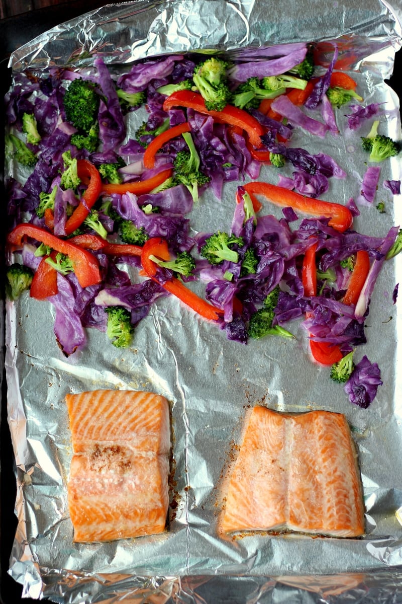 A foil-lined sheet pan with salmon and veggies on it.