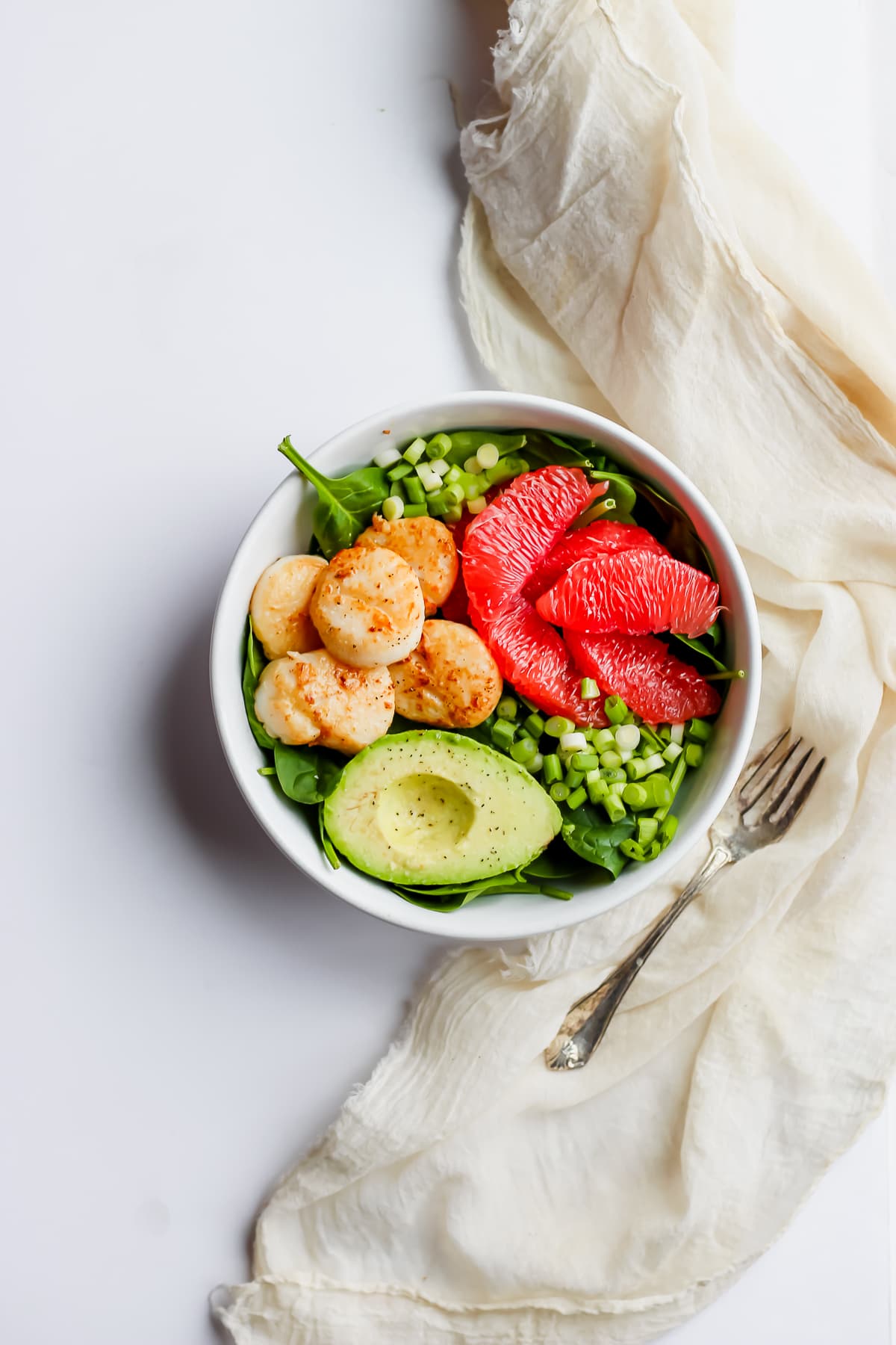 A scallop salad in a white bowl with a fork on the side.