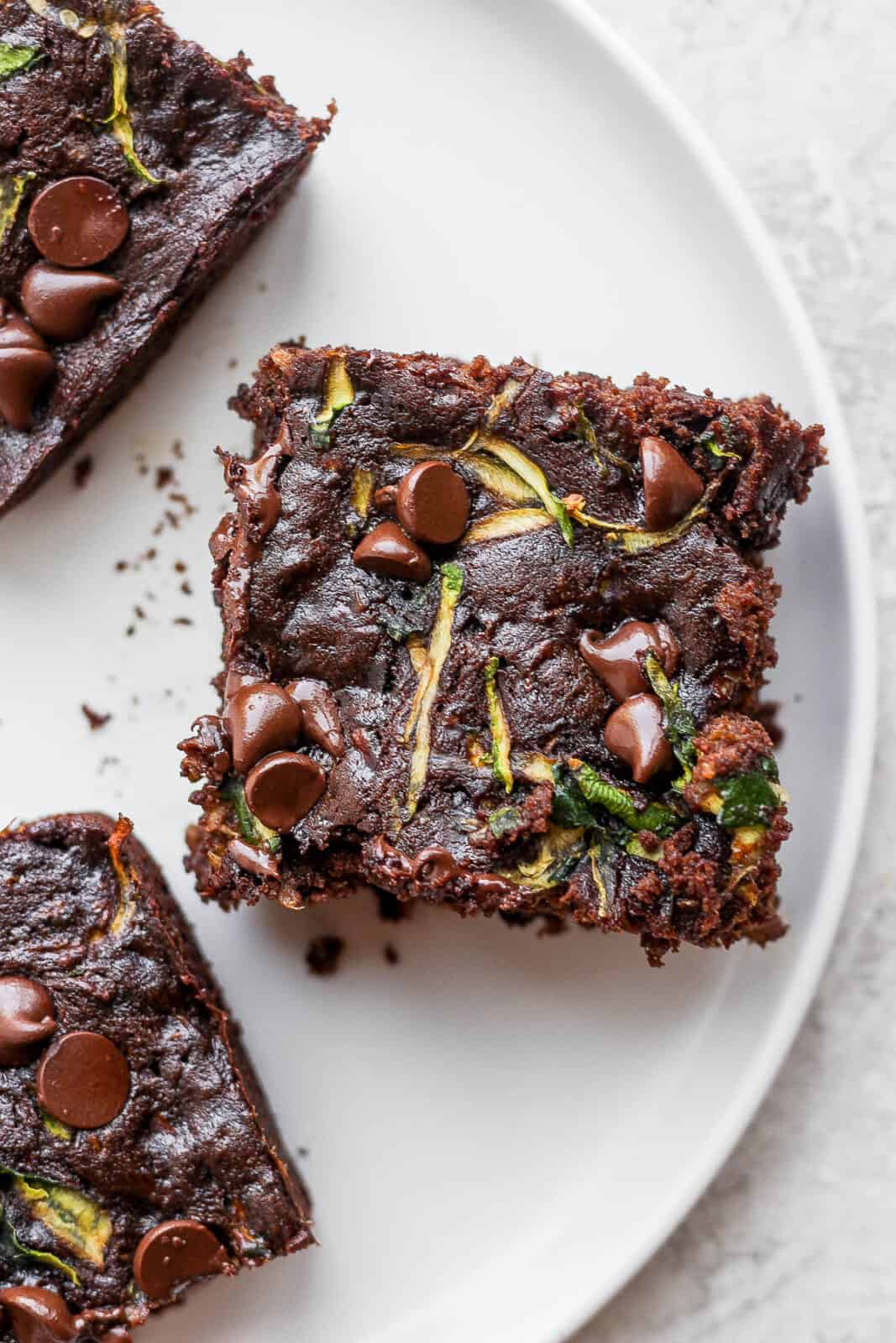 Three zucchini brownies on a plate. 