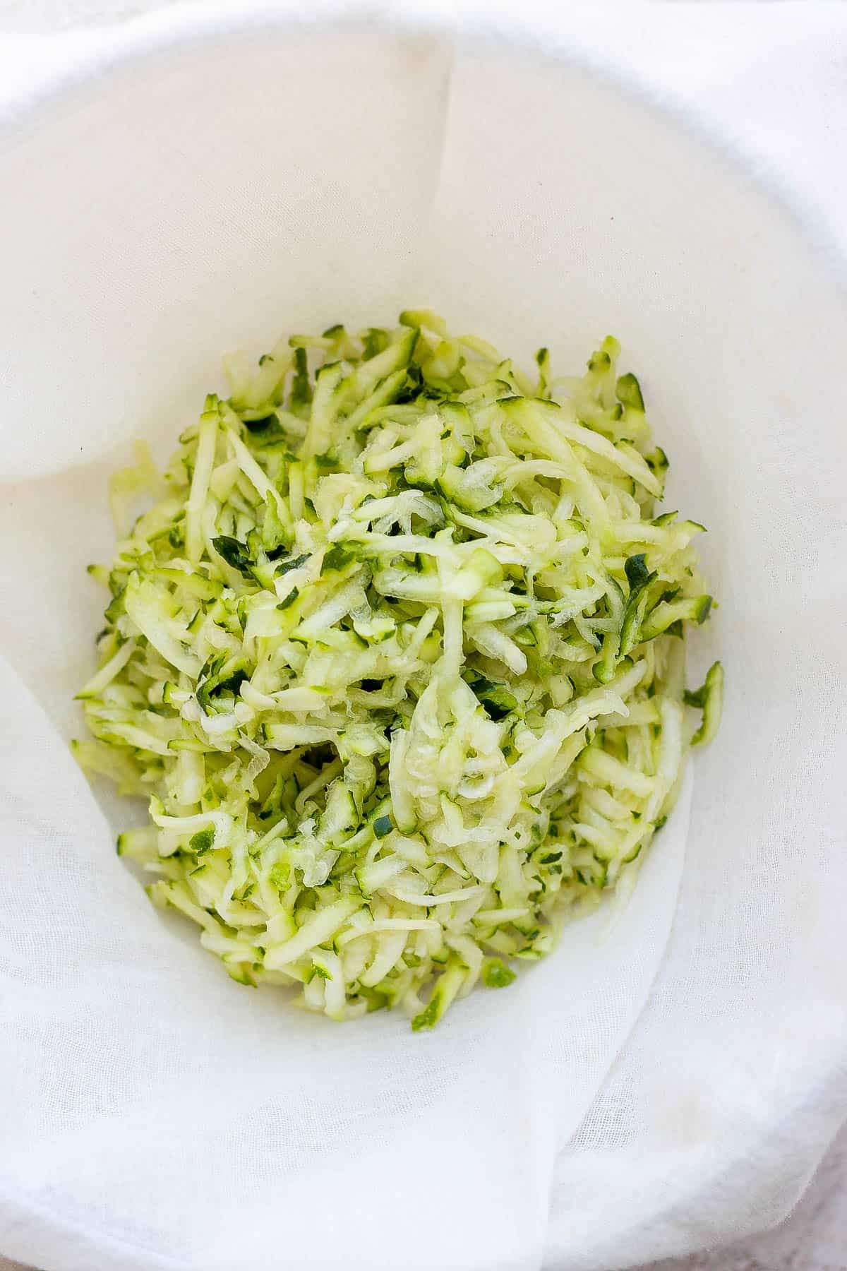 Shredded zucchini on top of cheesecloth. 