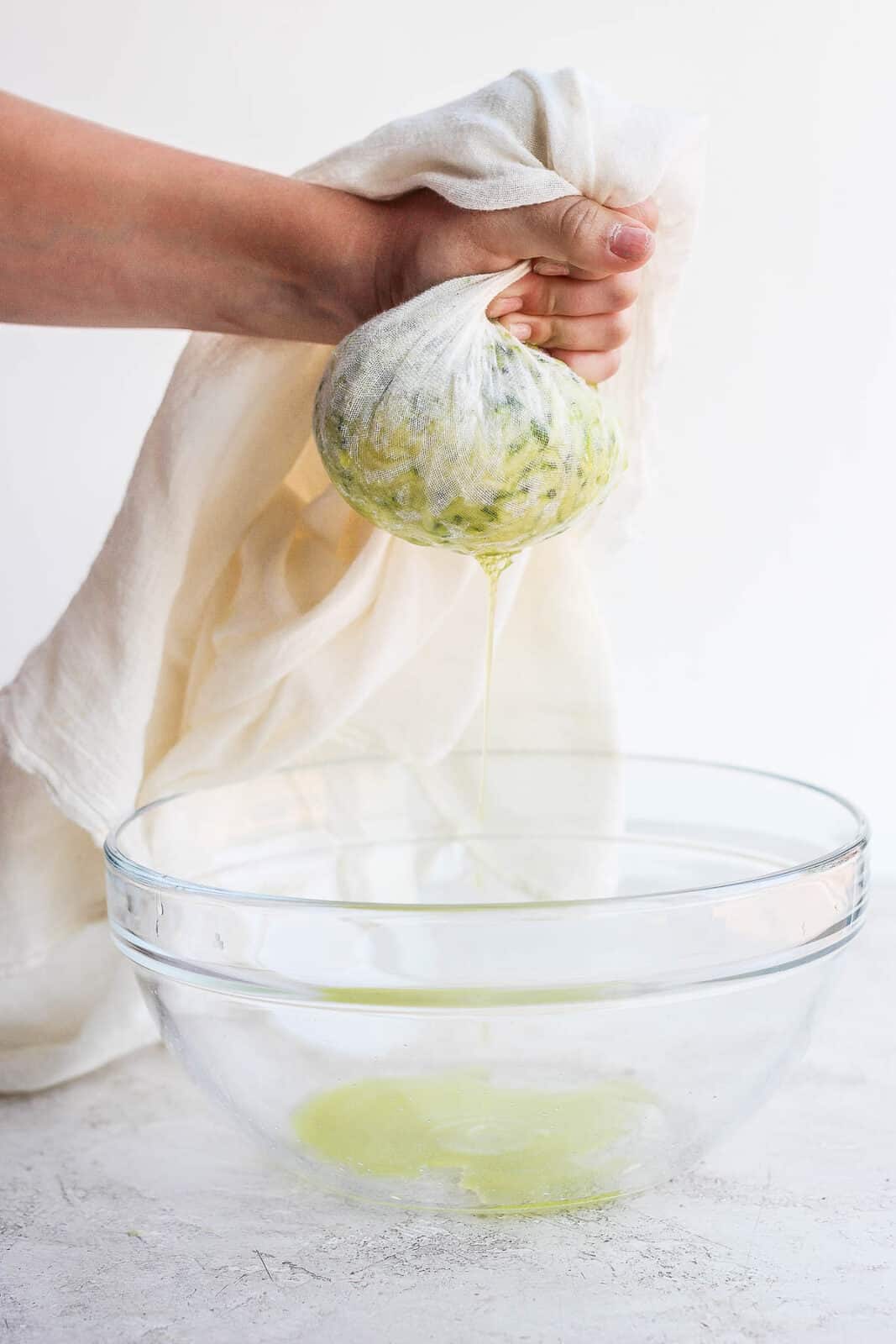 Someone squeezing shredded zucchini inside a cheesecloth to remove the excess moisture. 