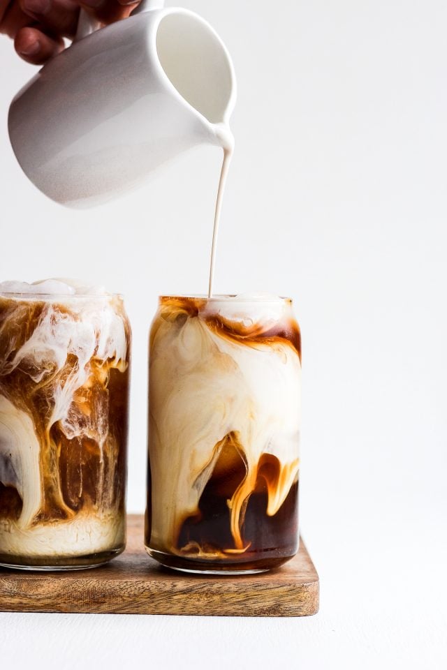 Someone pouring creamer into a glass of cold brew coffee. 