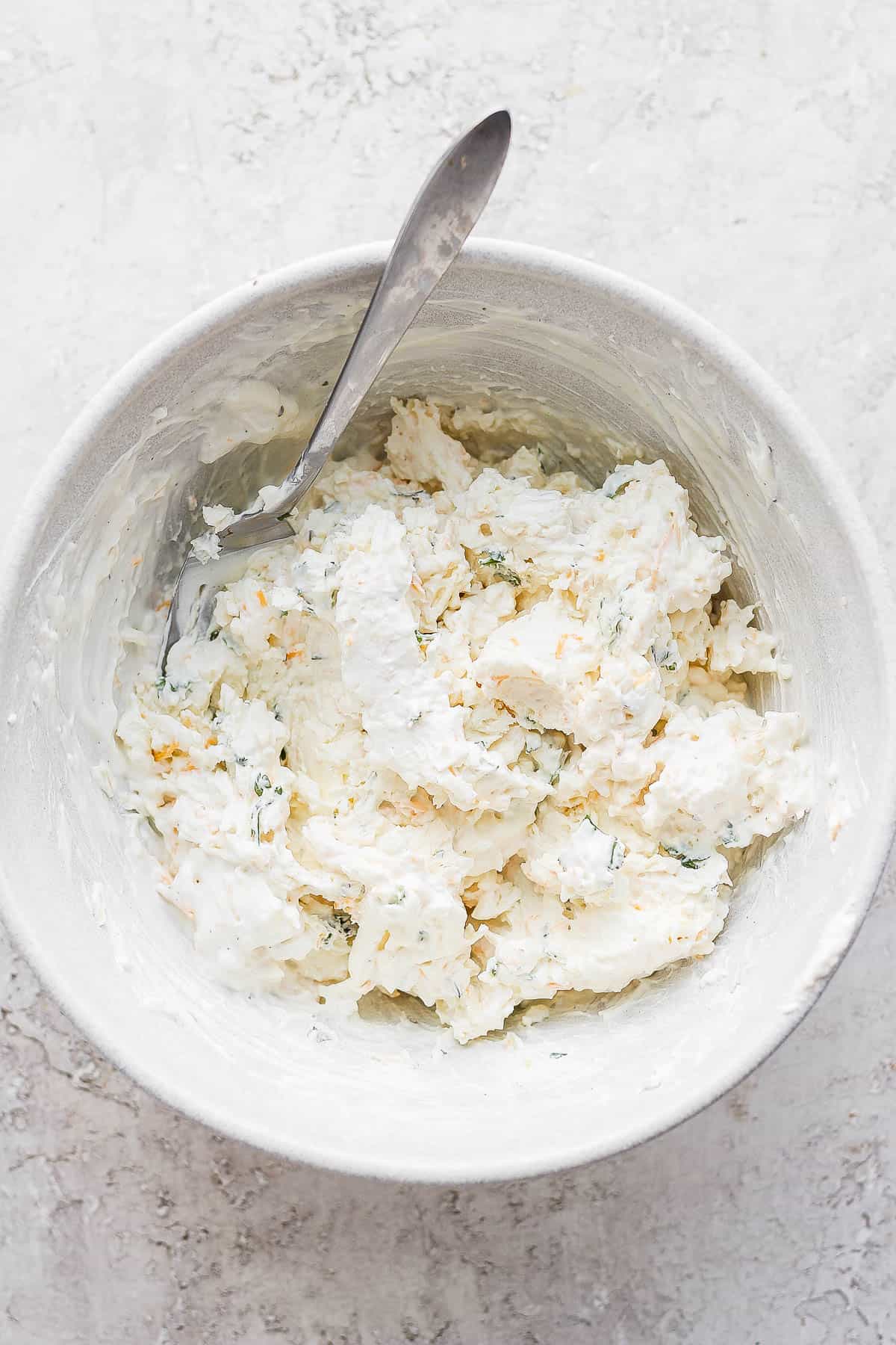 Cream cheese base ingredients in a bowl; mixed together with a spoon sticking out. 