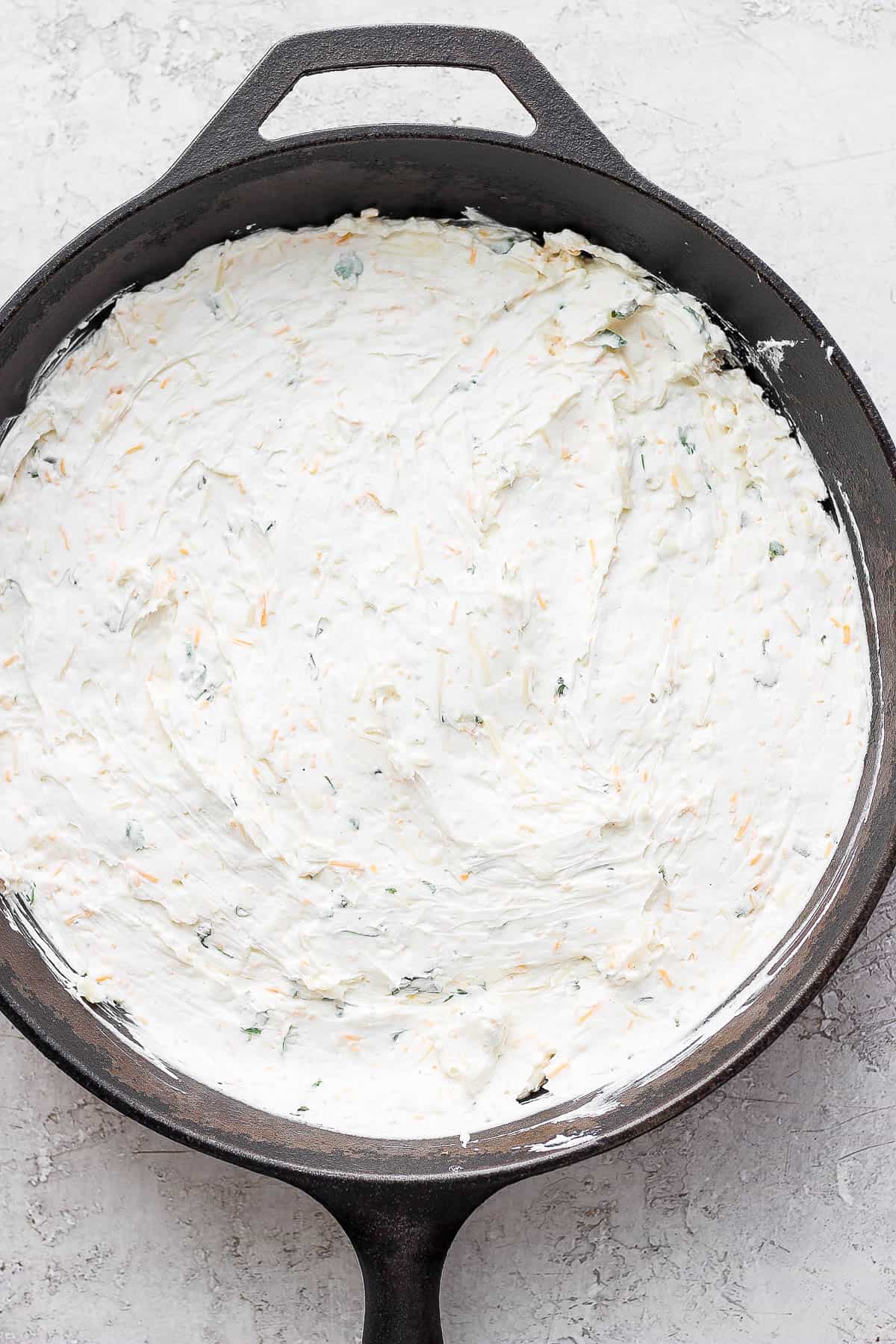 Cream cheese mixture spread out evenly in a cast iron skillet. 