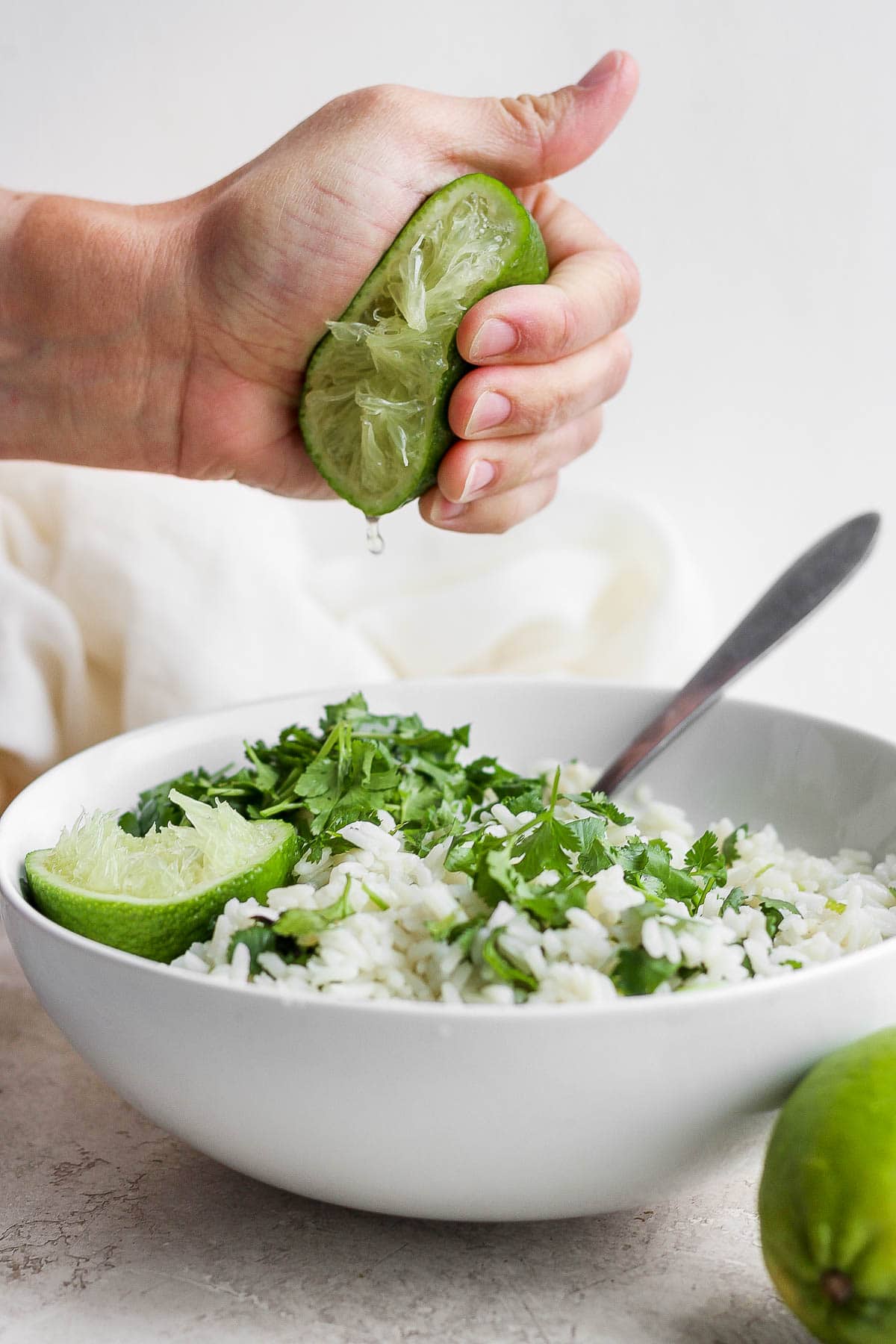 A hand squeezing a fresh lime into a bowl of cilantro lime rice. 