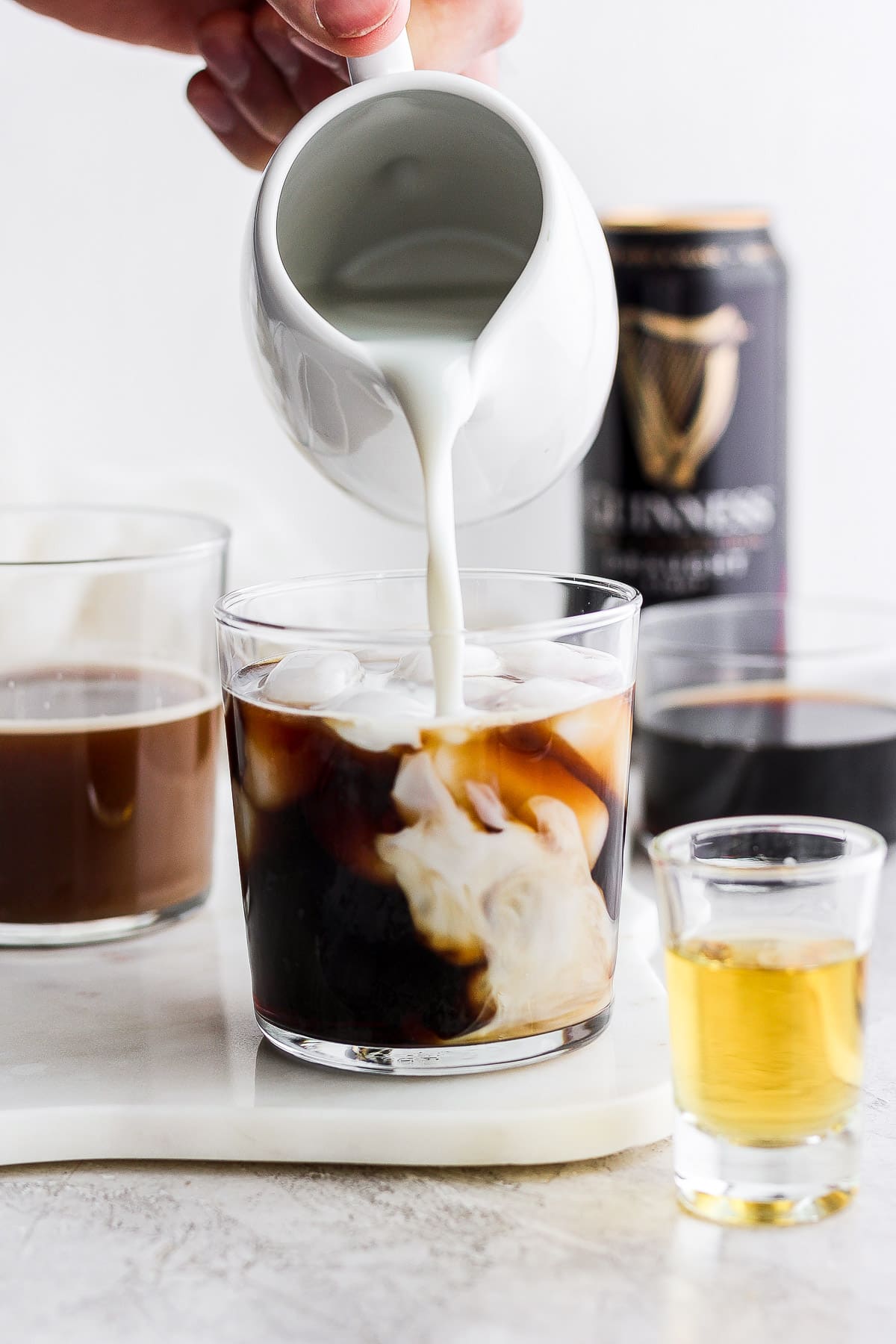 Dairy-free creamer being poured into a glass of cold brew coffee with a Guiness in the background. 
