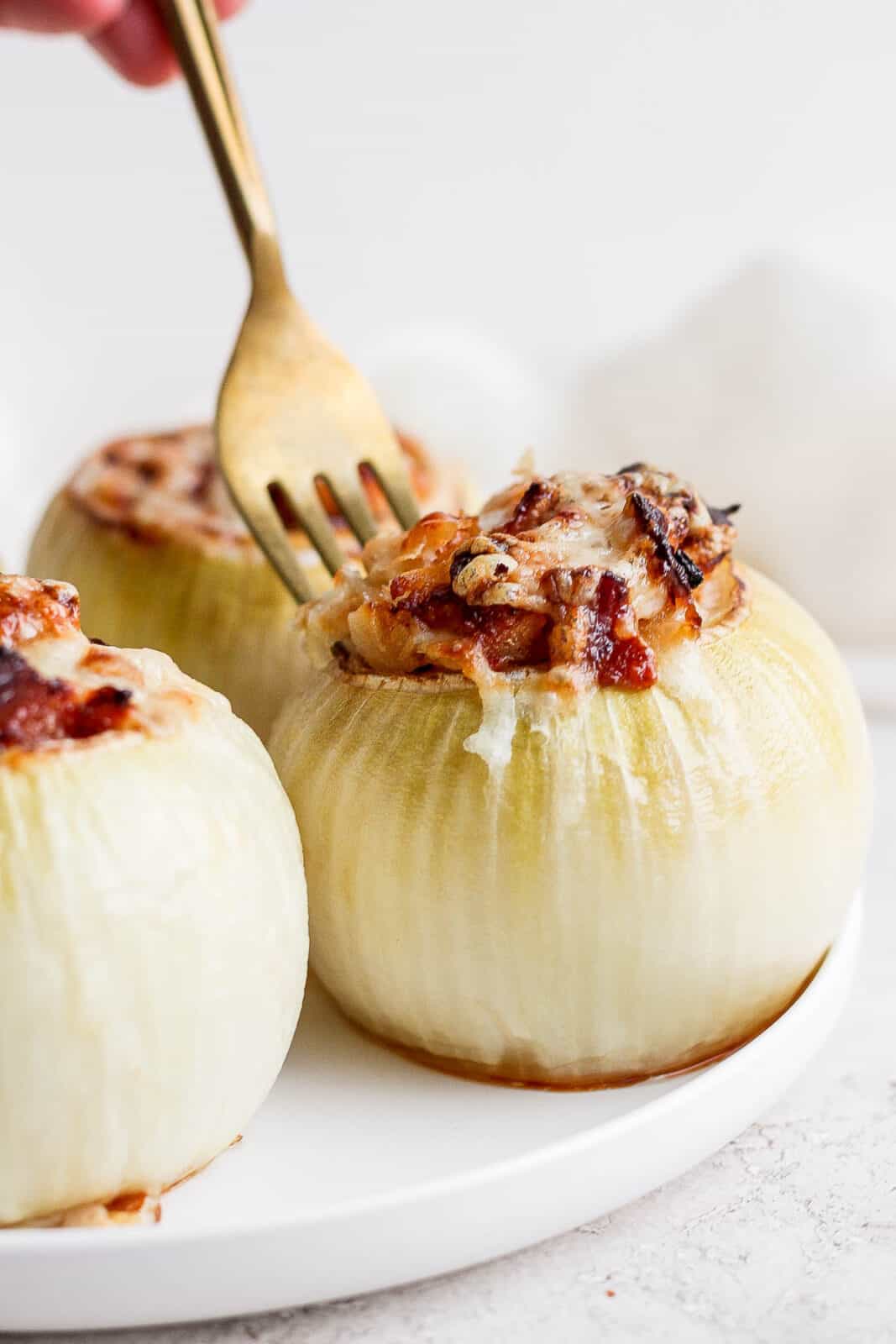 A plate of stuffed onions with a fork taking some of the stuffing out of an onion. 