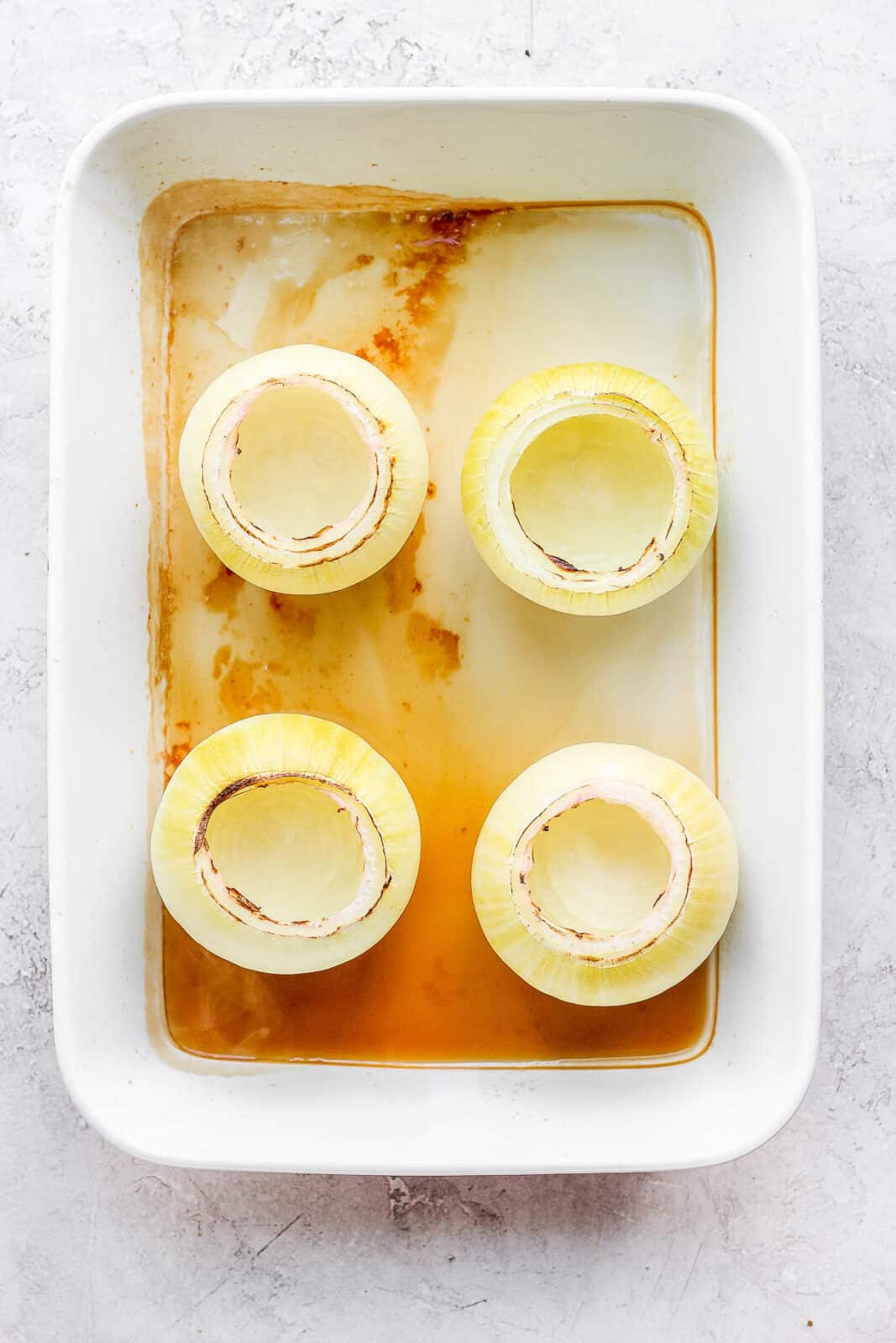 A baking pan with four baked, hollowed out onions.