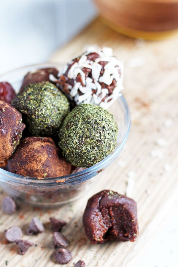 A variety of chocolate energy balls in a glass bowl with another energy ball sitting next to it.