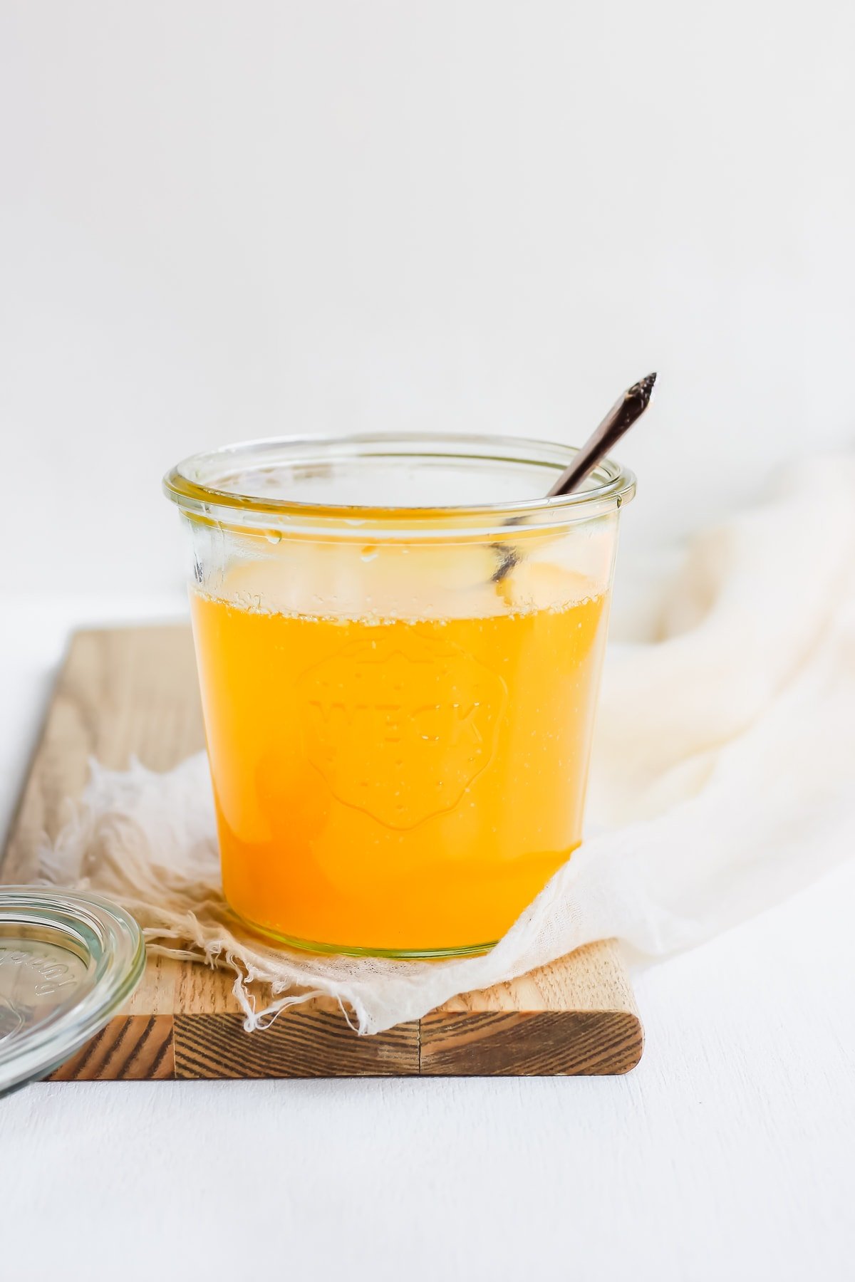 A weck jar full of liquid, homemade ghee sitting on a wooden board with a spoon sticking out.