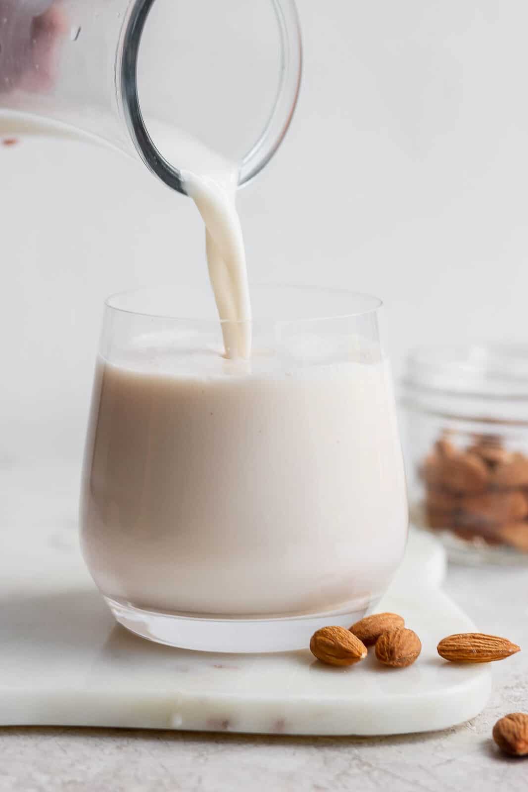 Someone pouring homemade almond milk into a glass. 