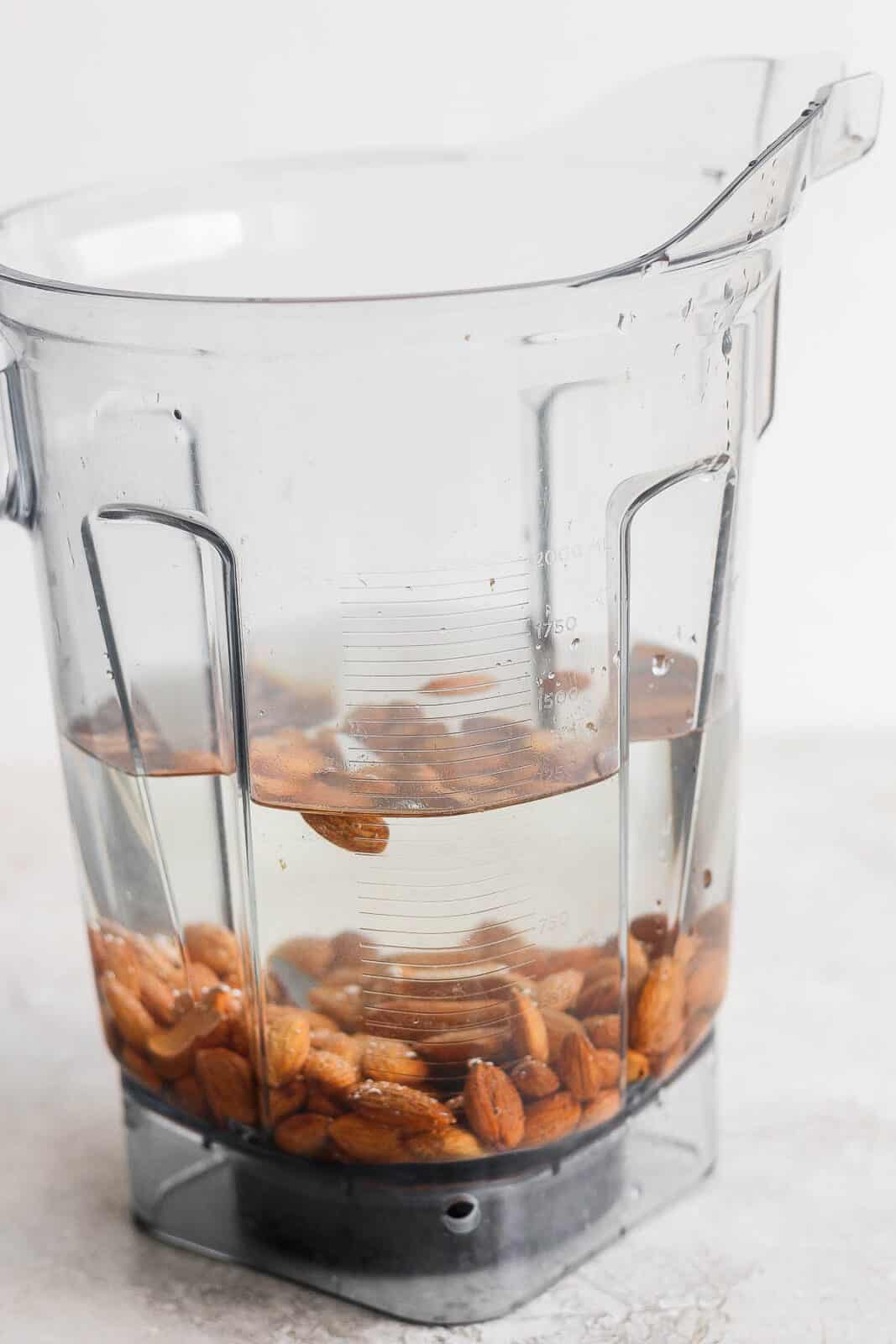 Raw almonds in a blender with water; side view.