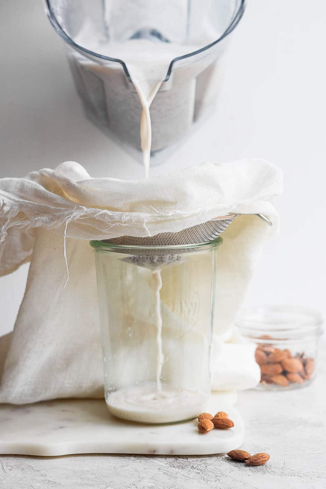 Someone straining almond milk through a cheesecloth into a glass container. 