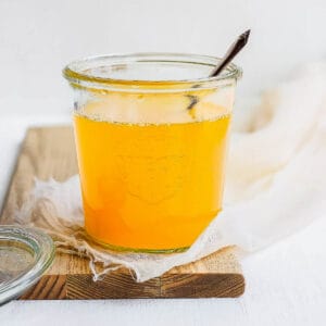 A weck jar full of liquid, homemade ghee sitting on a wooden board with a spoon sticking out.