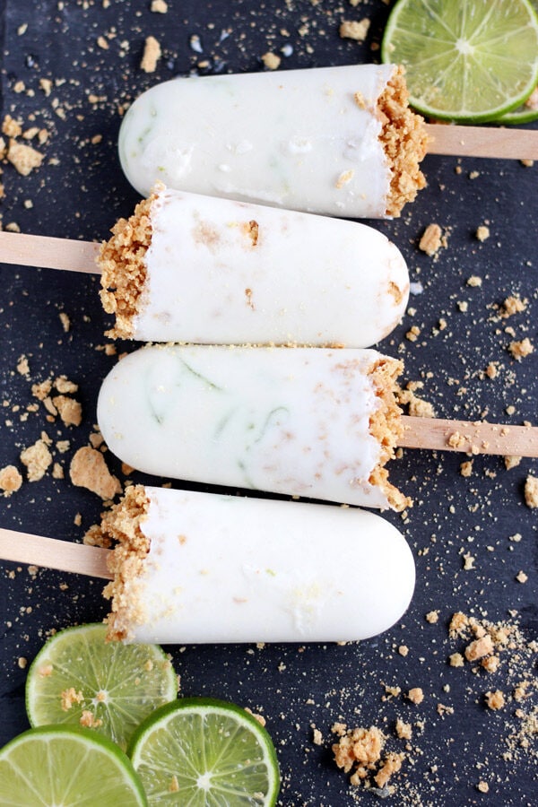 Four coconut key lime pie popsicles next to each other with graham cracker crumbs around them.