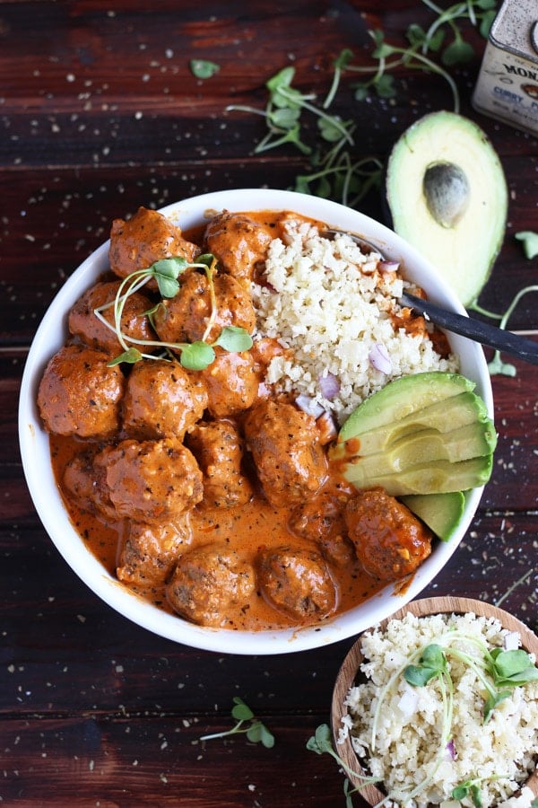 Curried meatballs in a white bowl with cauliflower rice and sliced avocado.