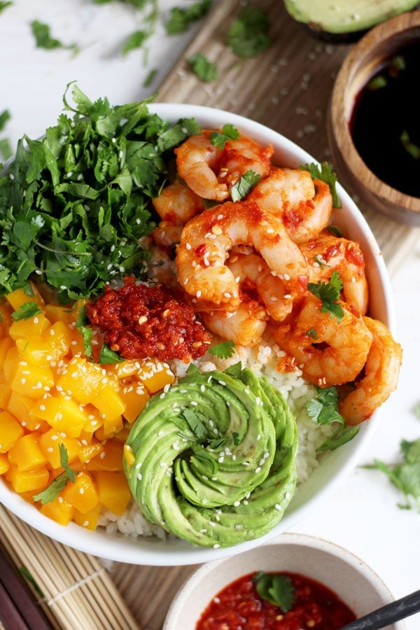 A white bowl with rice, spicy shrimp, avocado, mango, and cilantro.