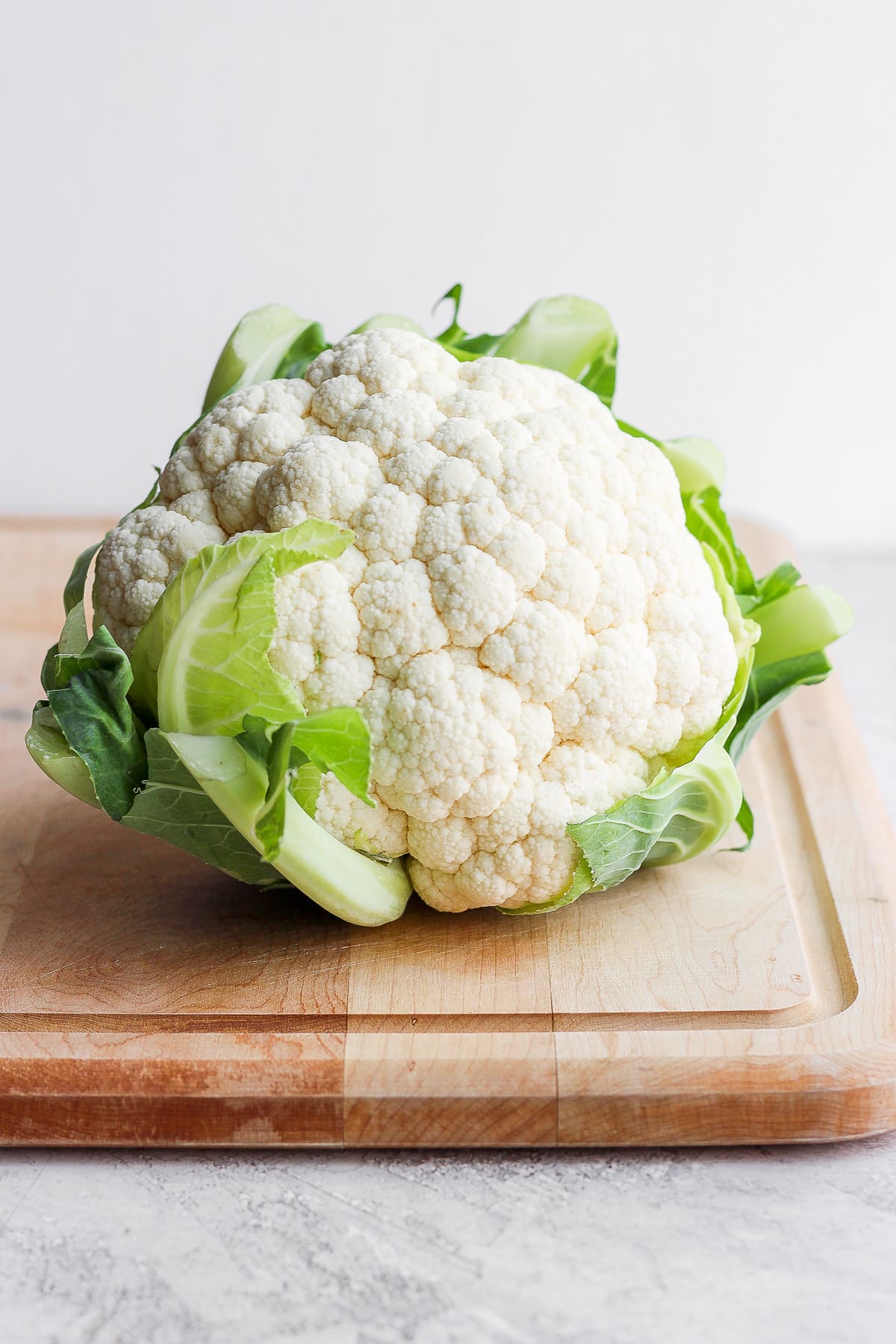 A head of cauliflower sitting on a cutting board. 