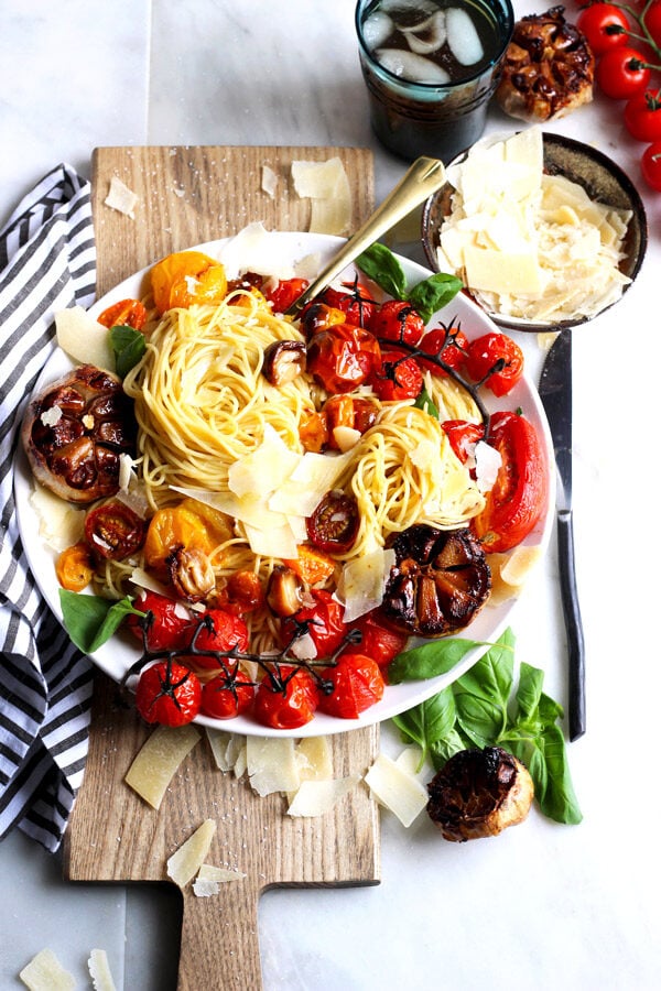 A deconstructed bow of roasted garlic marinara with noodles and fresh parmesan cheese shavings on top, with more in the bowl next to it.