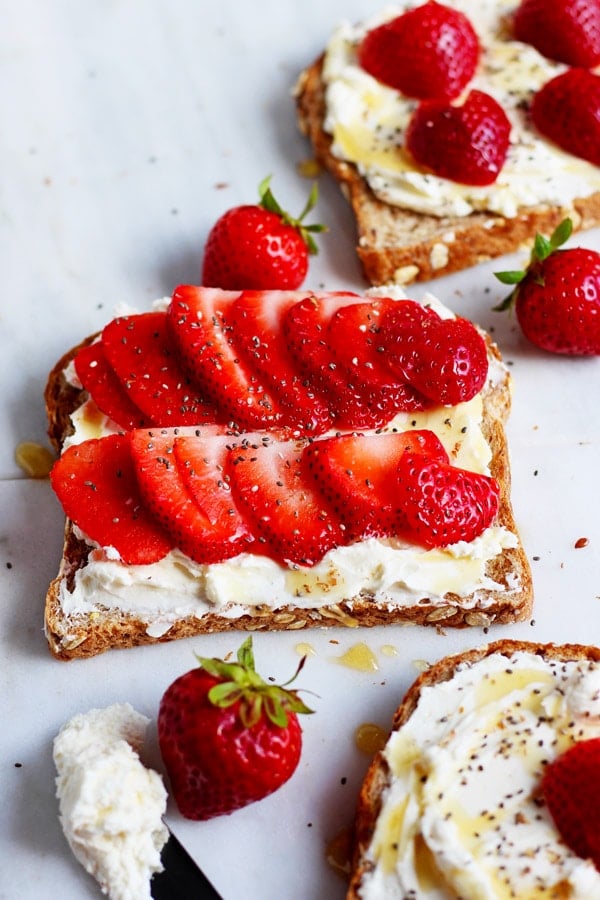 A fully topped slice of cream cheese toast next to a knife with cream cheese.