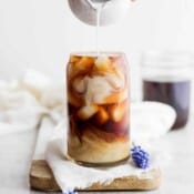 A lavender oat cold brew latte with oat milk being poured on top.