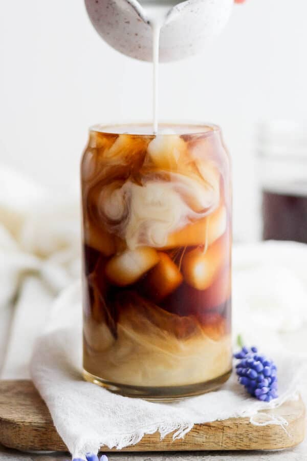 A lavender oat cold brew latte with oat milk being poured on top.