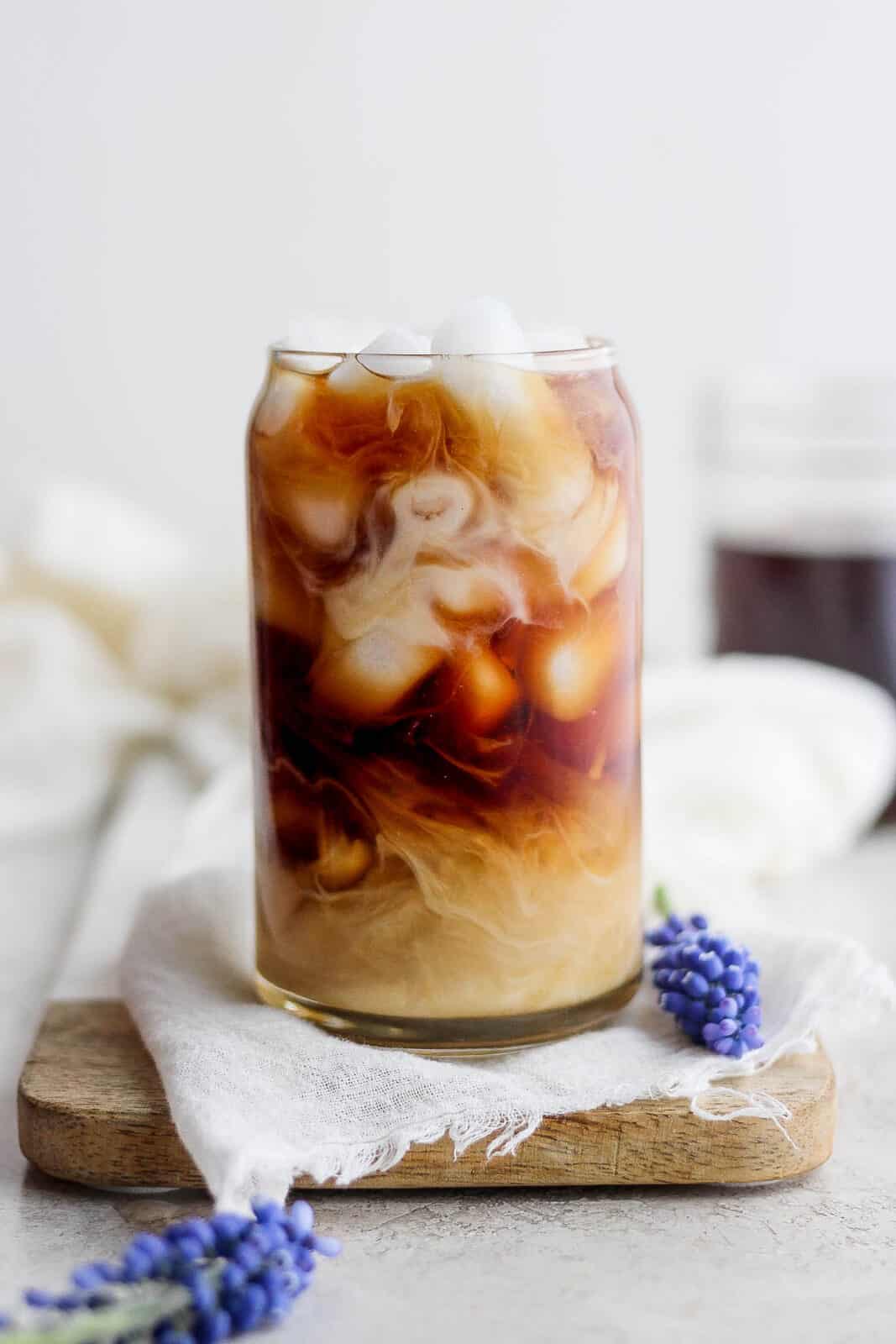 Glass of lavender cold brew with purple flowers next to it. 