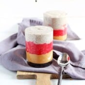 Two glasses of PB&J chia pudding on a wood board with a kitchen towel and spoon.