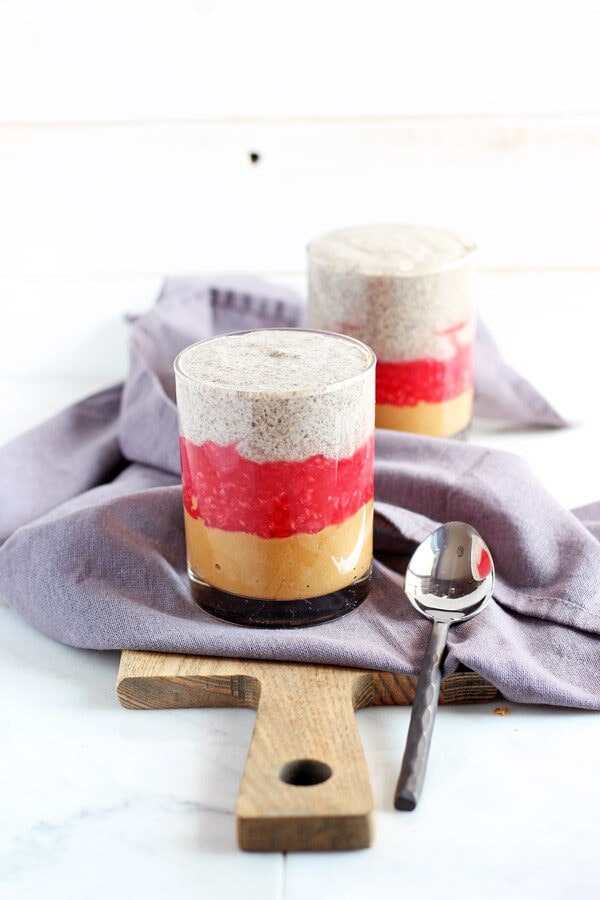 Two glasses of PB&J chia pudding on a wood board with a kitchen towel and spoon.