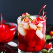 A glass of a fall cherry kombucha boulevardier with a bowl of cherries next to it.