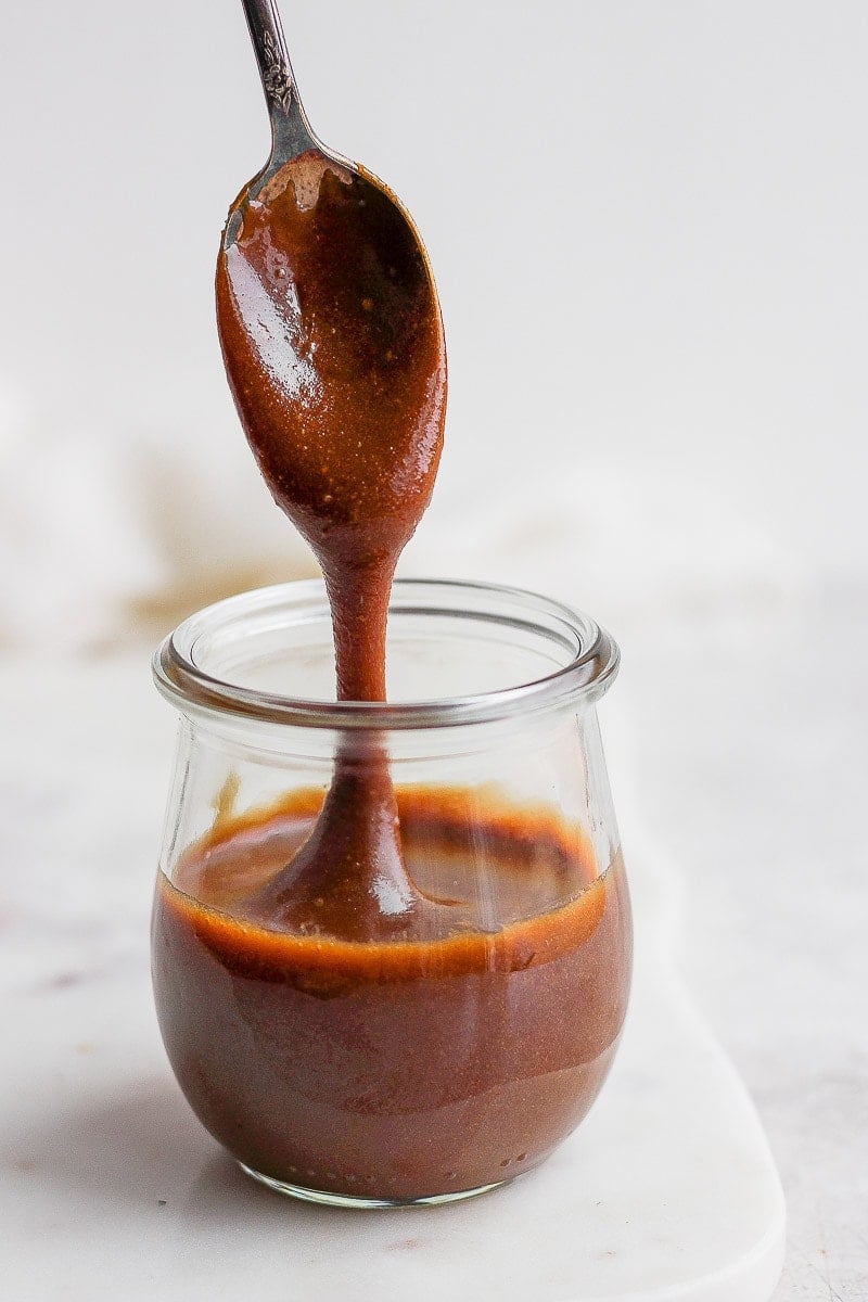 Jar of vegan caramel sauce with someone pulling a spoonful out. 