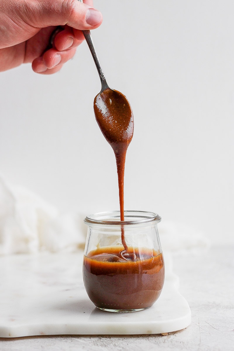 Jar of vegan caramel sauce with someone pulling a spoonful out. 