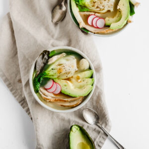 Two bowls of asian-inspired leftover turkey soup with a kitchen towel, spoon, and half an avocado.