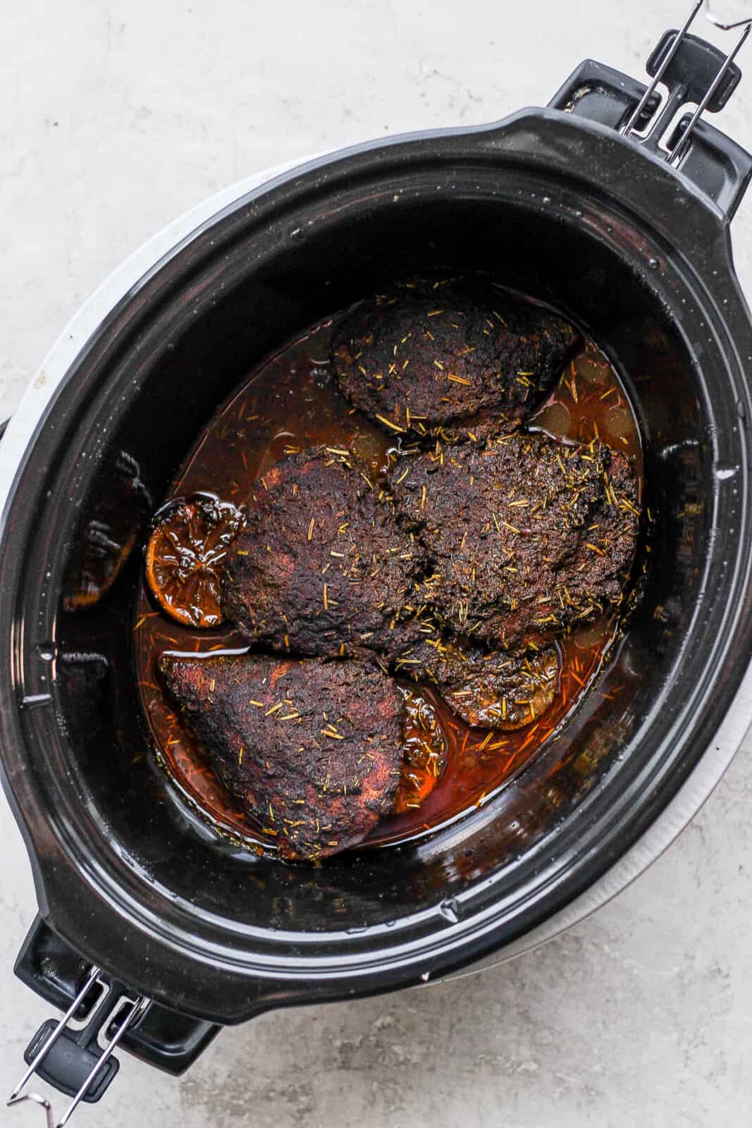 Four chicken breasts covered in jerk seasoning inside a slow cooker after cooking. 