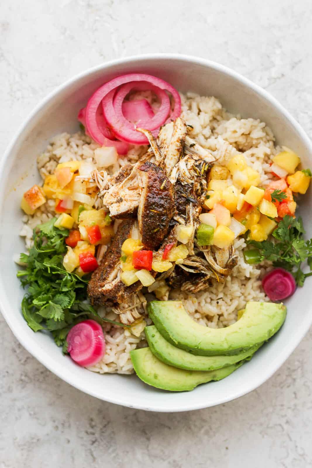 Bowl of crock pot jerk chicken with coconut rice, avocado and mango salsa. 