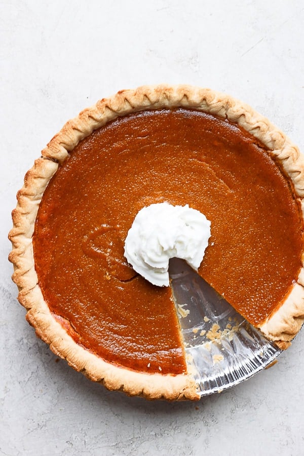 Dairy free pumpkin pie with whipped coconut cream in the center and a piece cut out. 