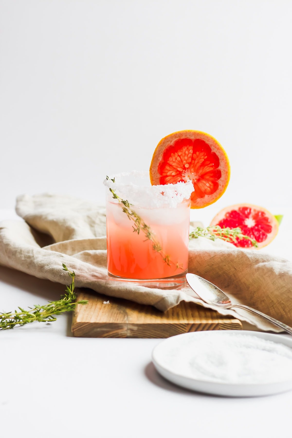 Garnished paloma mocktail in a glass next to a plate of salt.