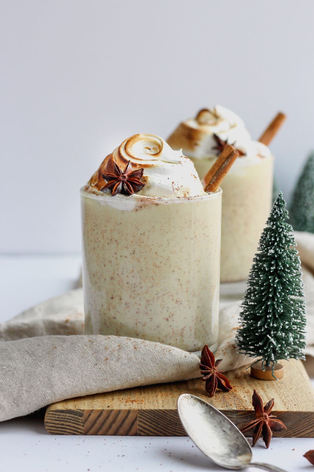 Two glasses of dairy free egg nog garnished with meringue and cinnamon stick. 