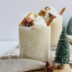 Two glasses of egg nog with cinnamon sticks out the top.