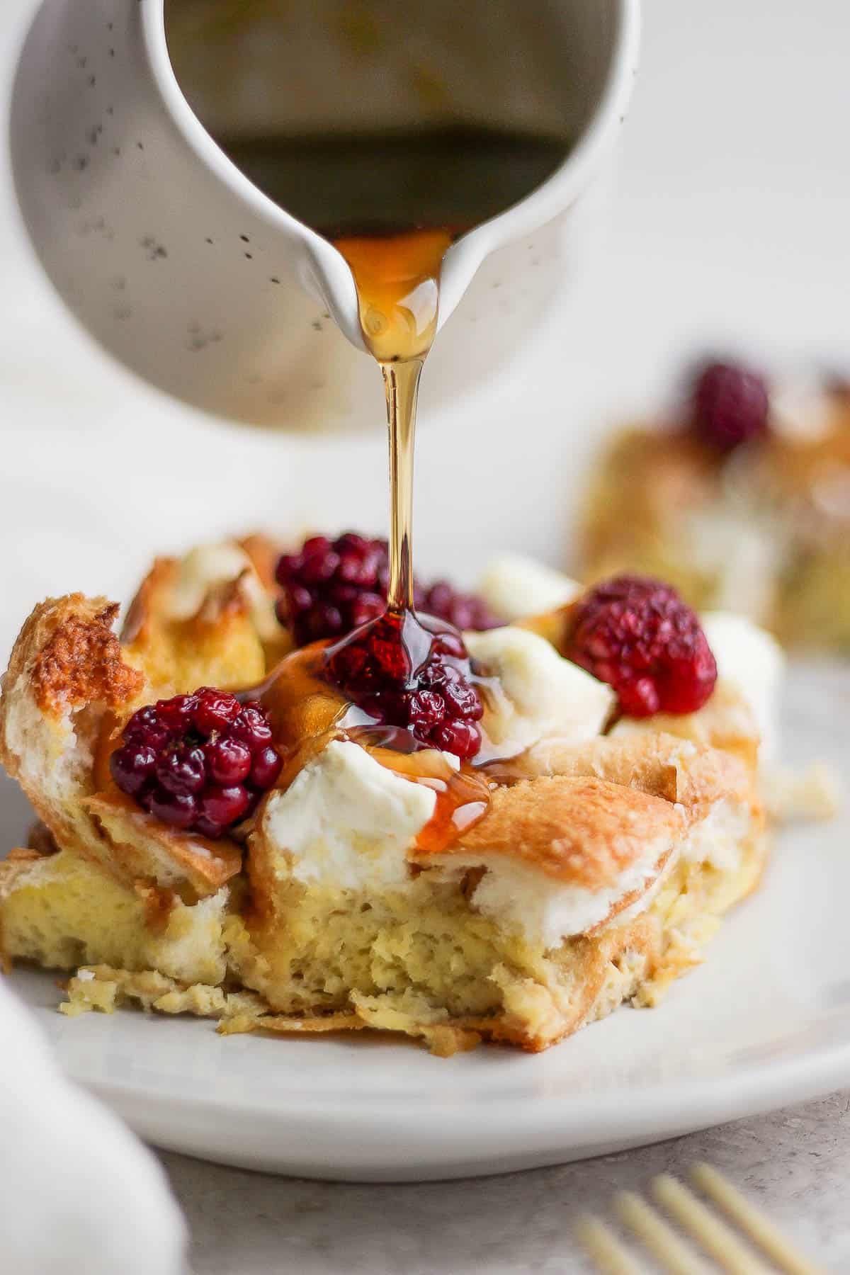 A piece of french toast bake on a plate and someone is drizzling maple syrup on top. 