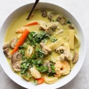 A white bowl with chicken and shrimp curry and a spoon.