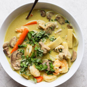 A white bowl with chicken and shrimp curry and a spoon.