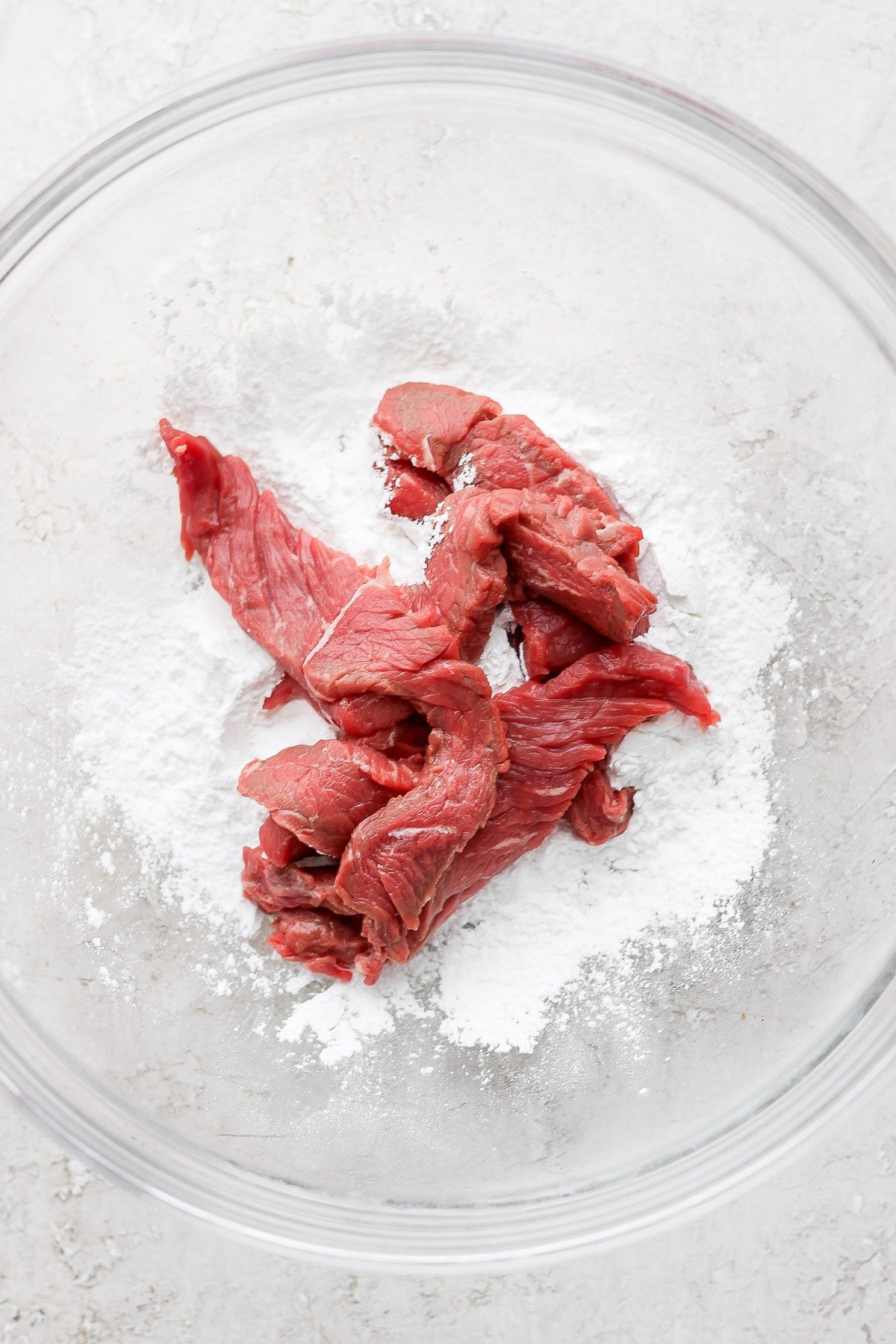 Lightly coating beef strips in arrowroot powder in a glass bowl. 