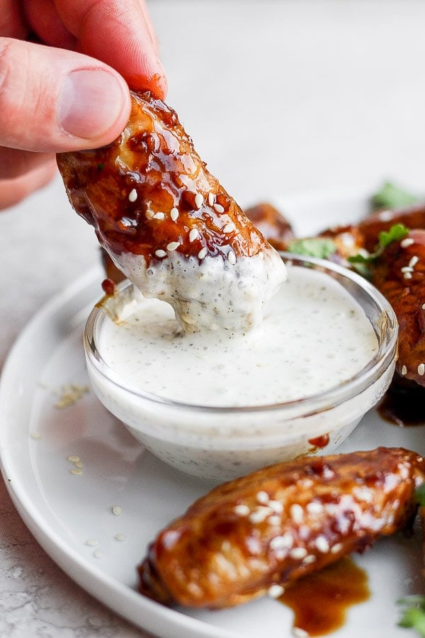 A male hand dipping a ginger sesame wing into some homemade ranch dressing. 