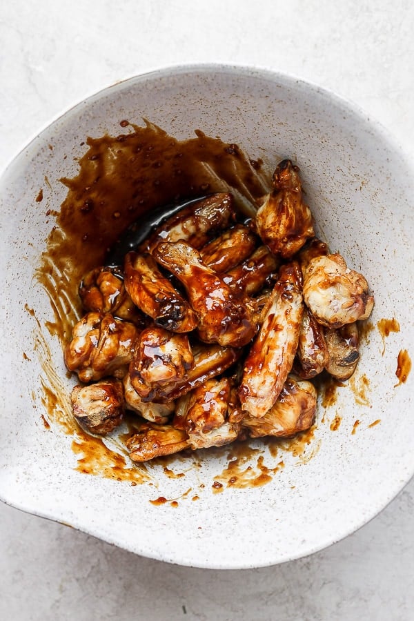 Baked wings in a large bowl with ginger sesame sauce poured on top. 