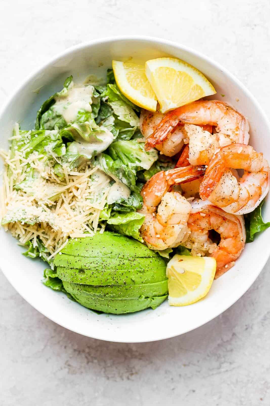 Bowl of shrimp caesar salad with avocado and parmesan cheese.