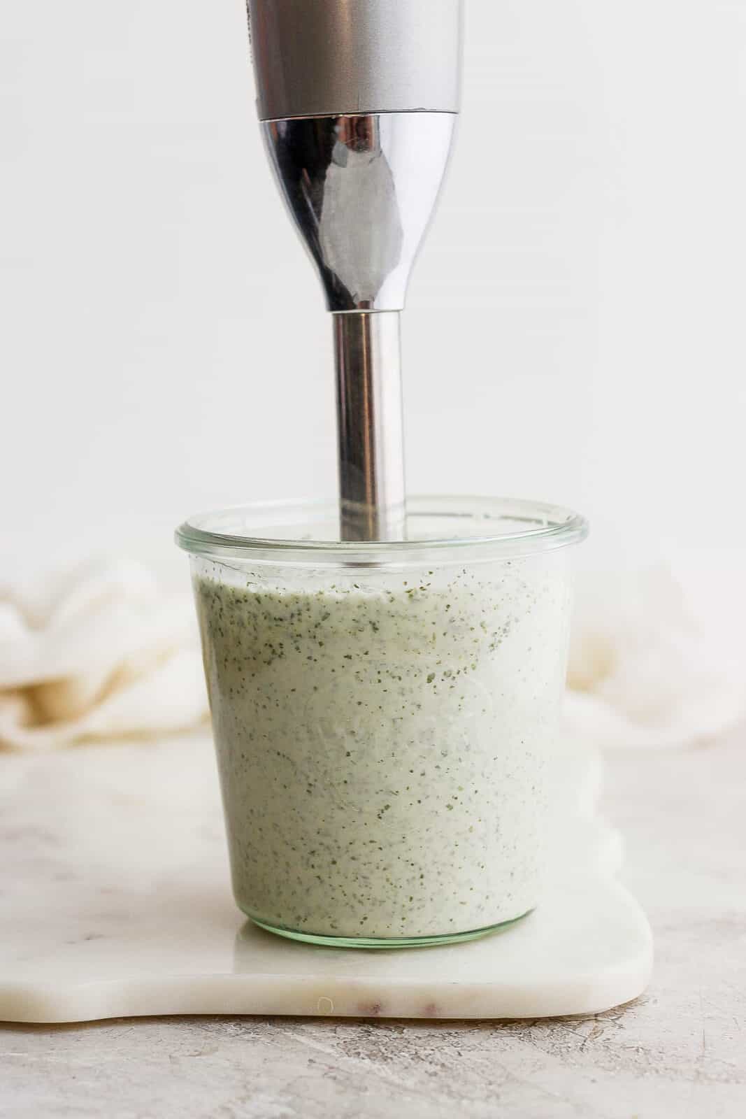 Someone mixing up a batch of dairy free ranch dressing in a weck jar using an immersion blender. 