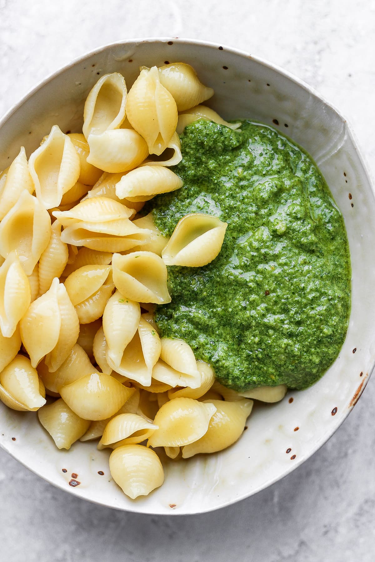 A bowl of cooked pasta shells and some vegan pesto. 